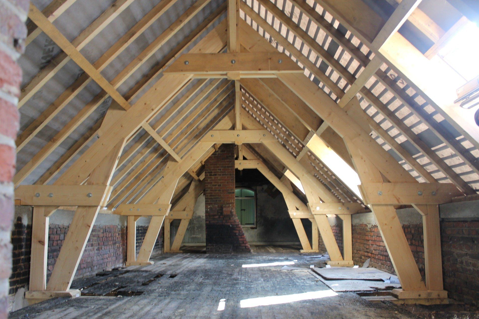 Combles non aménagés avec charpente apparente en bois clair, murs en briques et cheminée en briques visible.