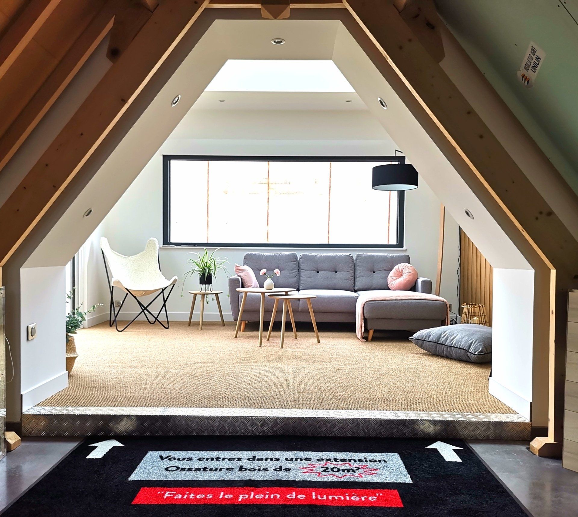 Un espace de vie en loft vu à travers un cadre triangulaire, avec un canapé gris, un fauteuil papillon et un tapis de sol coloré.
