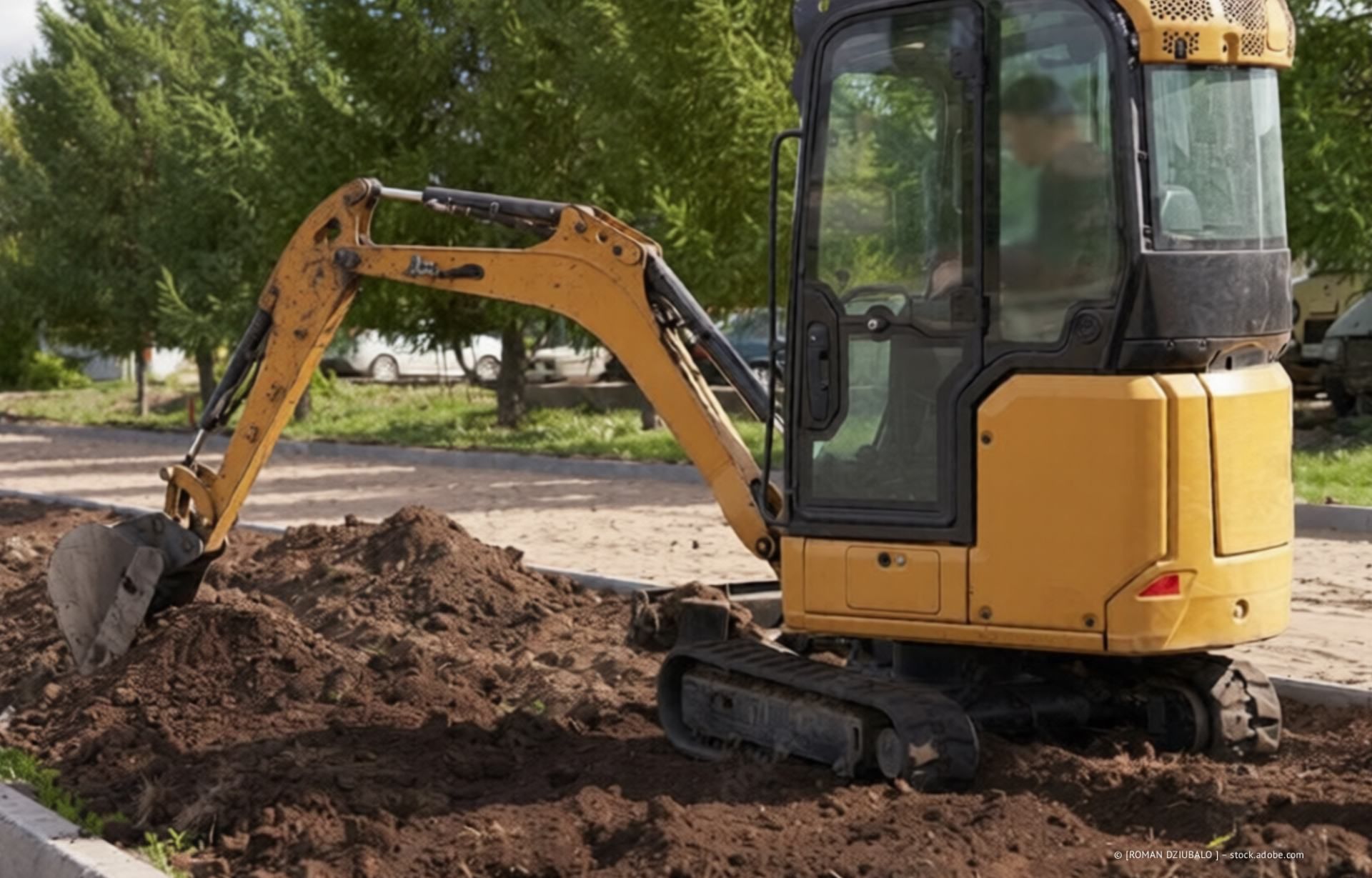 Ein roter Minibagger gräbt sich an einer Baustelle vor einem modernen Haus in die Erde.