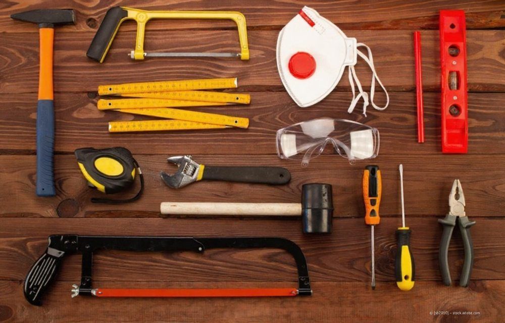 Verschiedene Werkzeuge, darunter Sägen, Hämmer, Schutzausrüstung und Messinstrumente, sind auf einer braunen Holzoberfläche angeordnet.