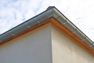 Coin d'un bâtiment blanc avec un toit en métal gris et des finitions orange sur fond de ciel nuageux