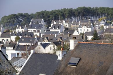 Toits de village et maisons à flanc de colline, avec une ligne d'arbres en arrière-plan.