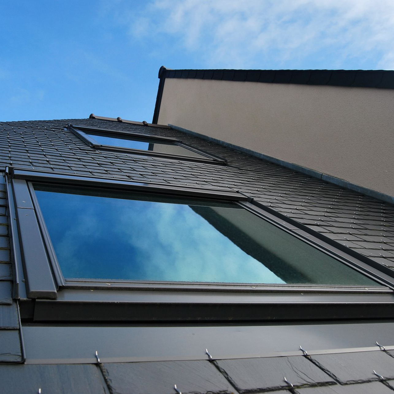 Vue en contre-plongée du toit d'une maison moderne avec une grande lucarne reflétant le ciel bleu