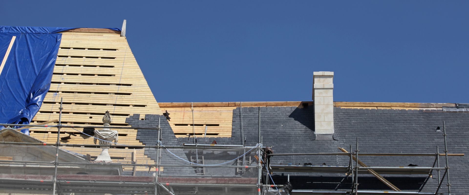 Toiture partiellement construite avec échafaudages, revêtement en bois, ardoises et cheminée.