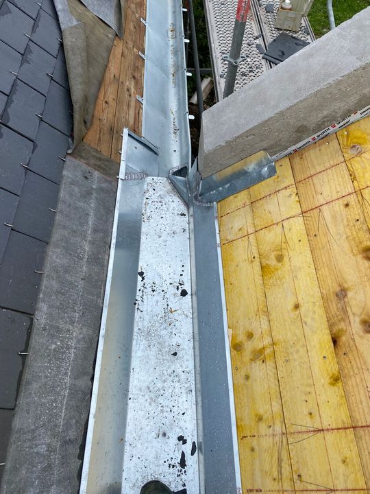 Zone de travail sur la toiture avec solins métalliques, bardeaux et revêtement jaune, à côté d'une gouttière.