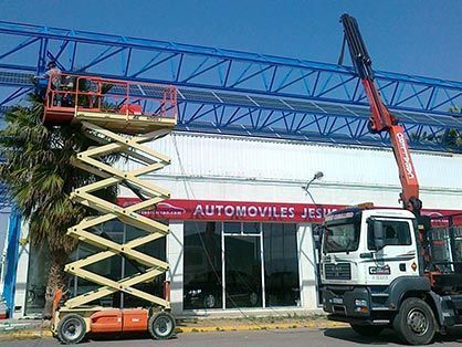 Un hombre está parado en un elevador de tijera frente a un edificio.