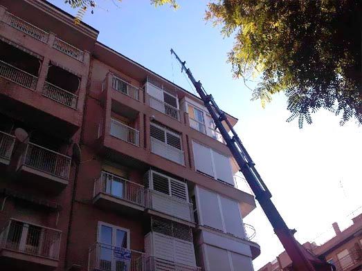 Una grúa roja está levantando un gran edificio con balcones.
