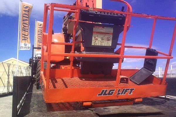 Un elevador Jlg naranja está estacionado frente a un edificio.