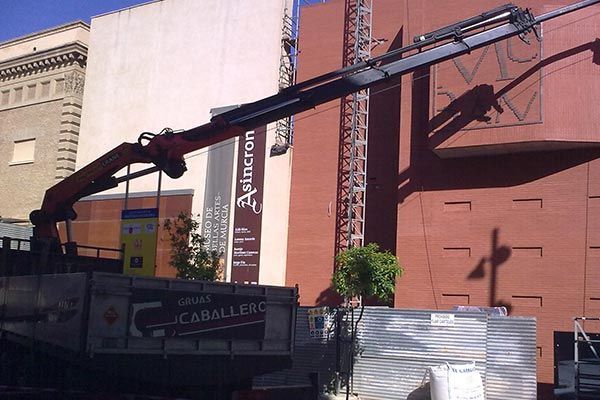 Un camión con una grúa acoplada está estacionado frente a un edificio que tiene escrito 