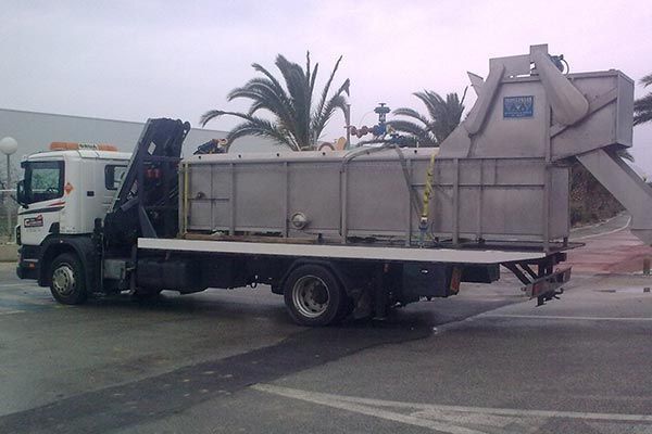 Un camión de basura está estacionado en un estacionamiento con palmeras al fondo.