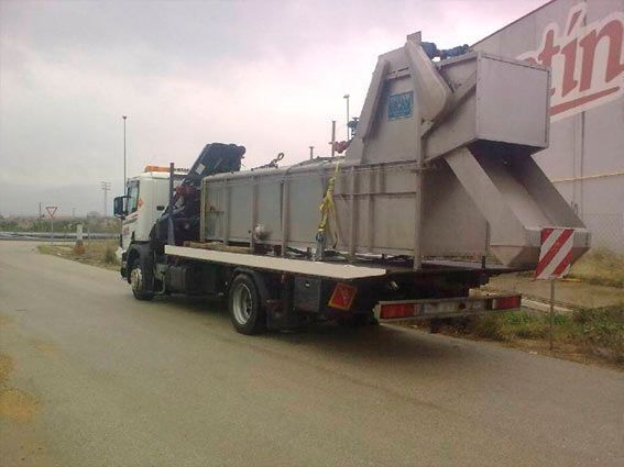 Una grúa con un gran contenedor en la parte trasera está estacionada al costado de la carretera.