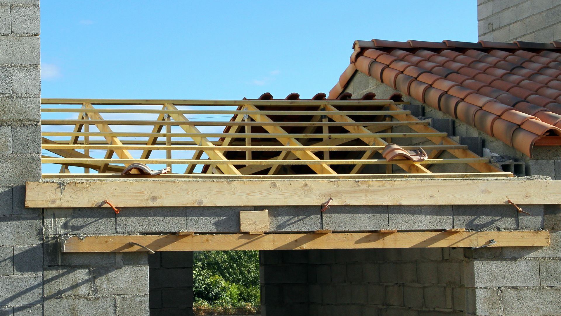 Fermes et poutres en bois visibles sur une structure en parpaings ; toit partiellement recouvert de tuiles en arrière-plan.