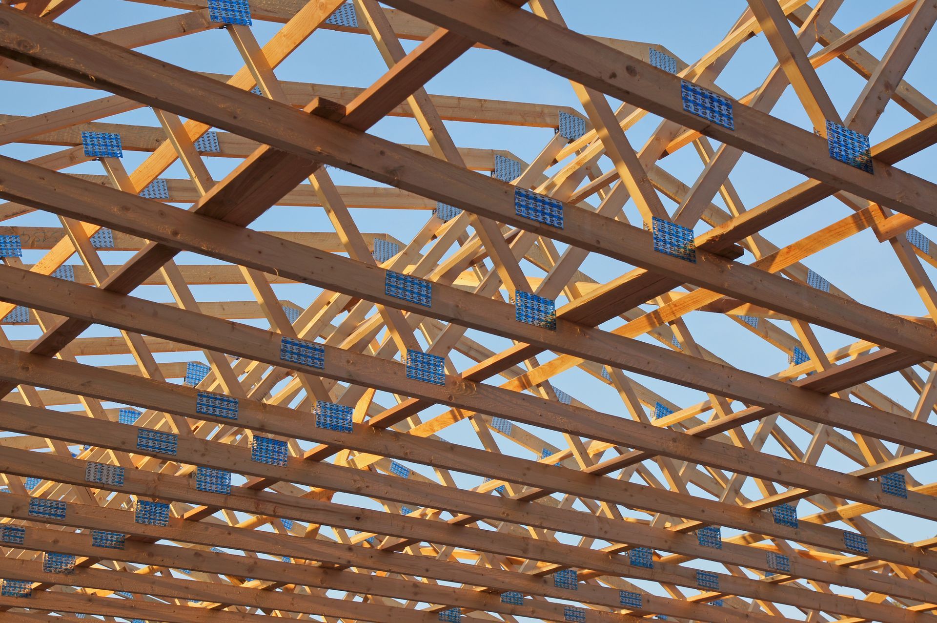 Charpente de toit en bois avec connecteurs métalliques, sur fond de ciel bleu.