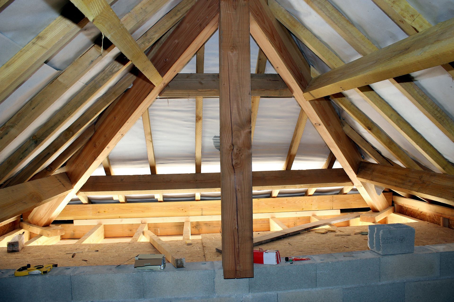 Vue intérieure d'une charpente de combles en bois, comprenant les chevrons, un poteau central et l'isolation.