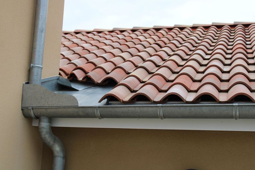 Toiture en tuiles de terre cuite avec système de gouttières métalliques.