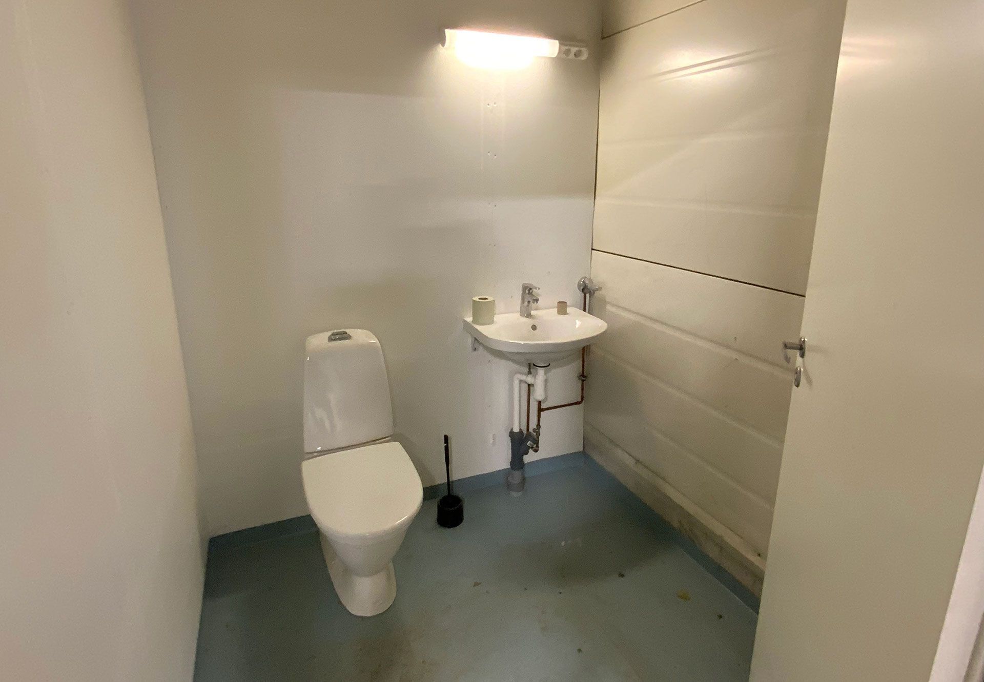Pieni, perusjulkinen wc, jossa on wc-istuin, pesuallas ja valo. Valkoiset seinät ja sininen lattia.