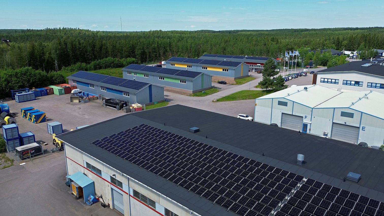 Ilmakuva: Aurinkopaneelit tehtaiden katoilla puiden ympäröimänä.