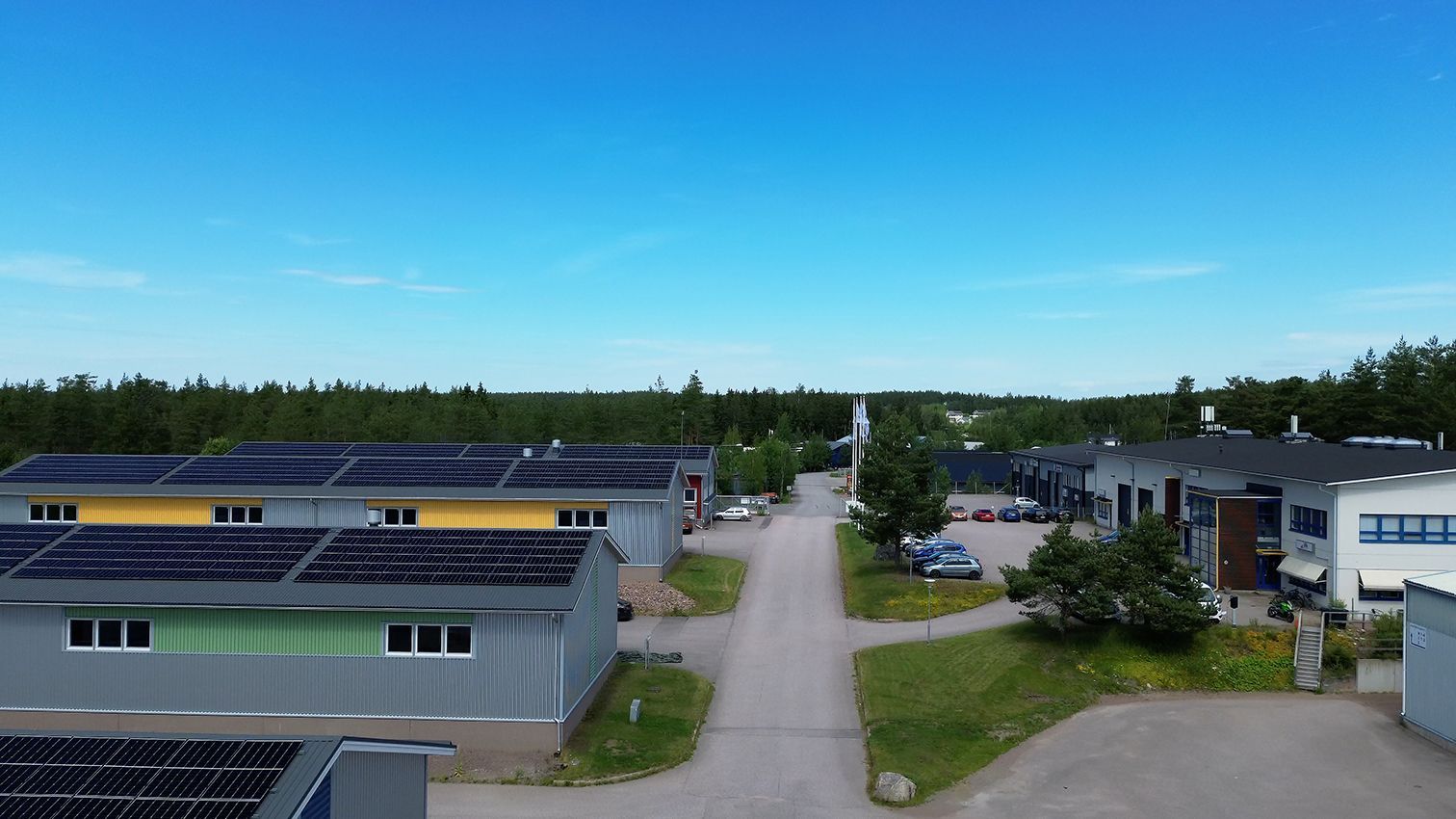 Asuinrakennuksia, joiden katoilla on aurinkopaneelit, tie, puita ja sininen taivas.