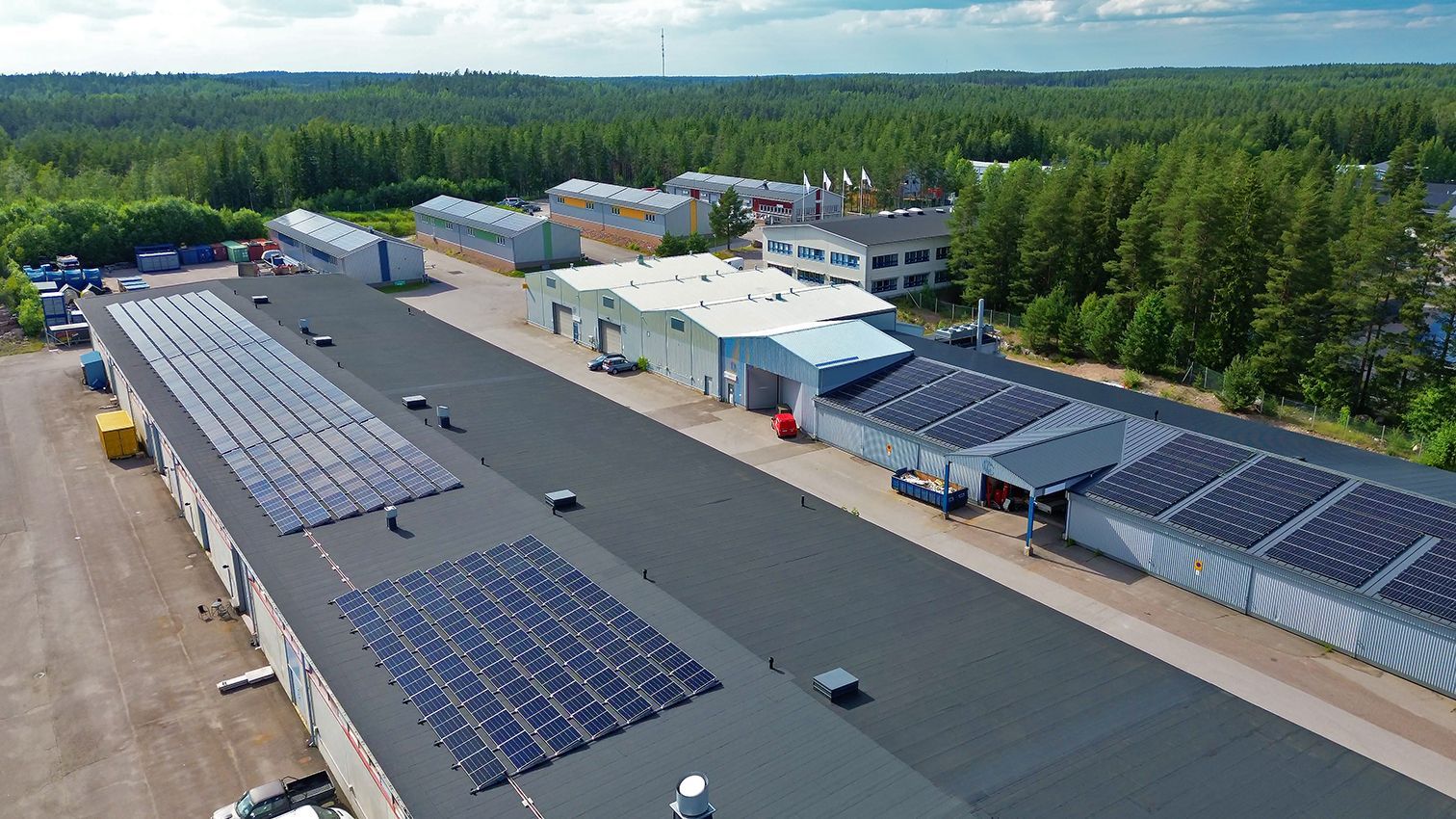 Ilmakuva teollisuusrakennuksista, joiden katoilla on aurinkopaneelit, puiden ympäröimänä.