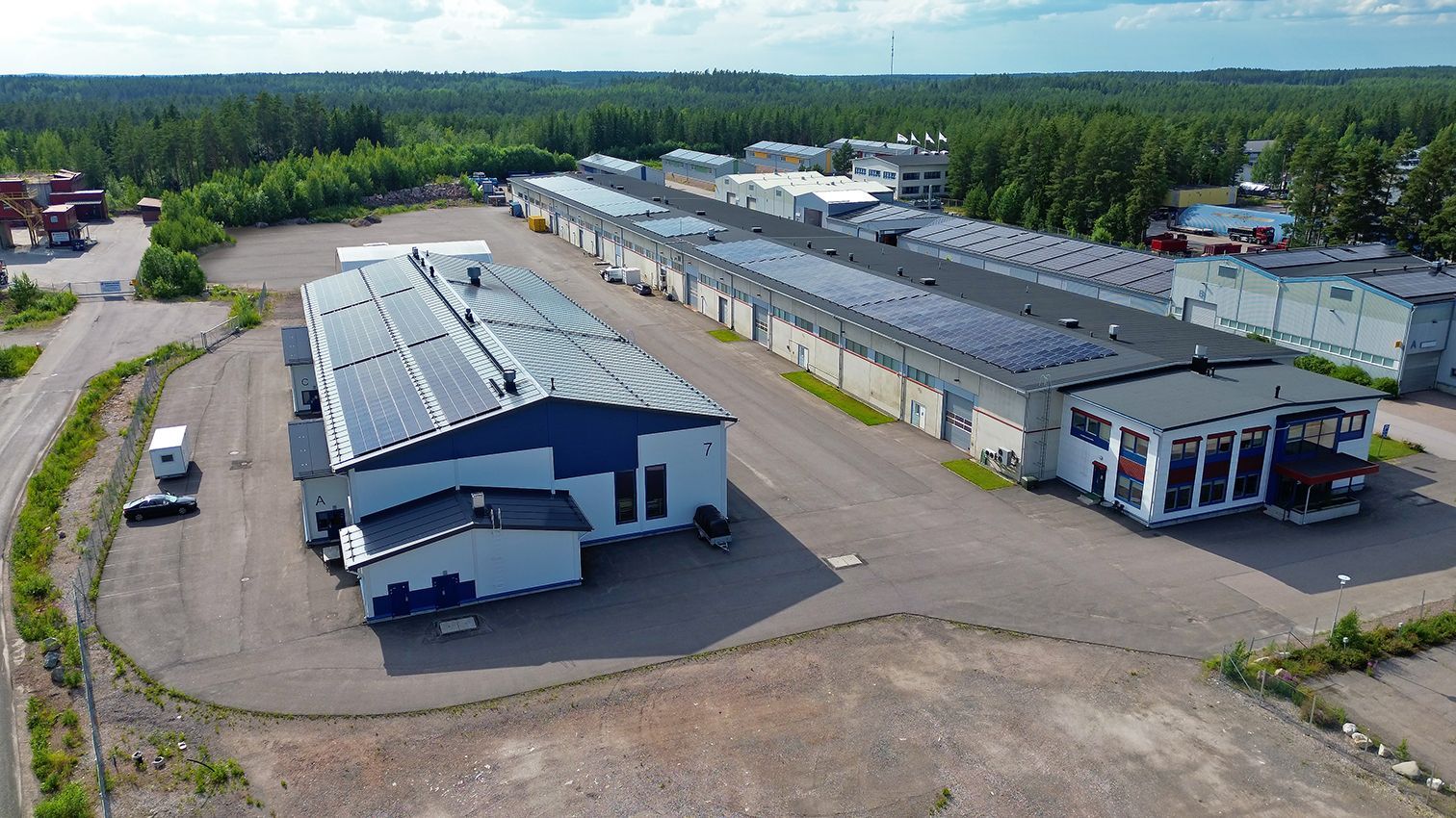 Ilmakuva teollisuusrakennuksista, joissa on aurinkopaneelit ja joita ympäröivät puiden ympäröimät rakennukset.