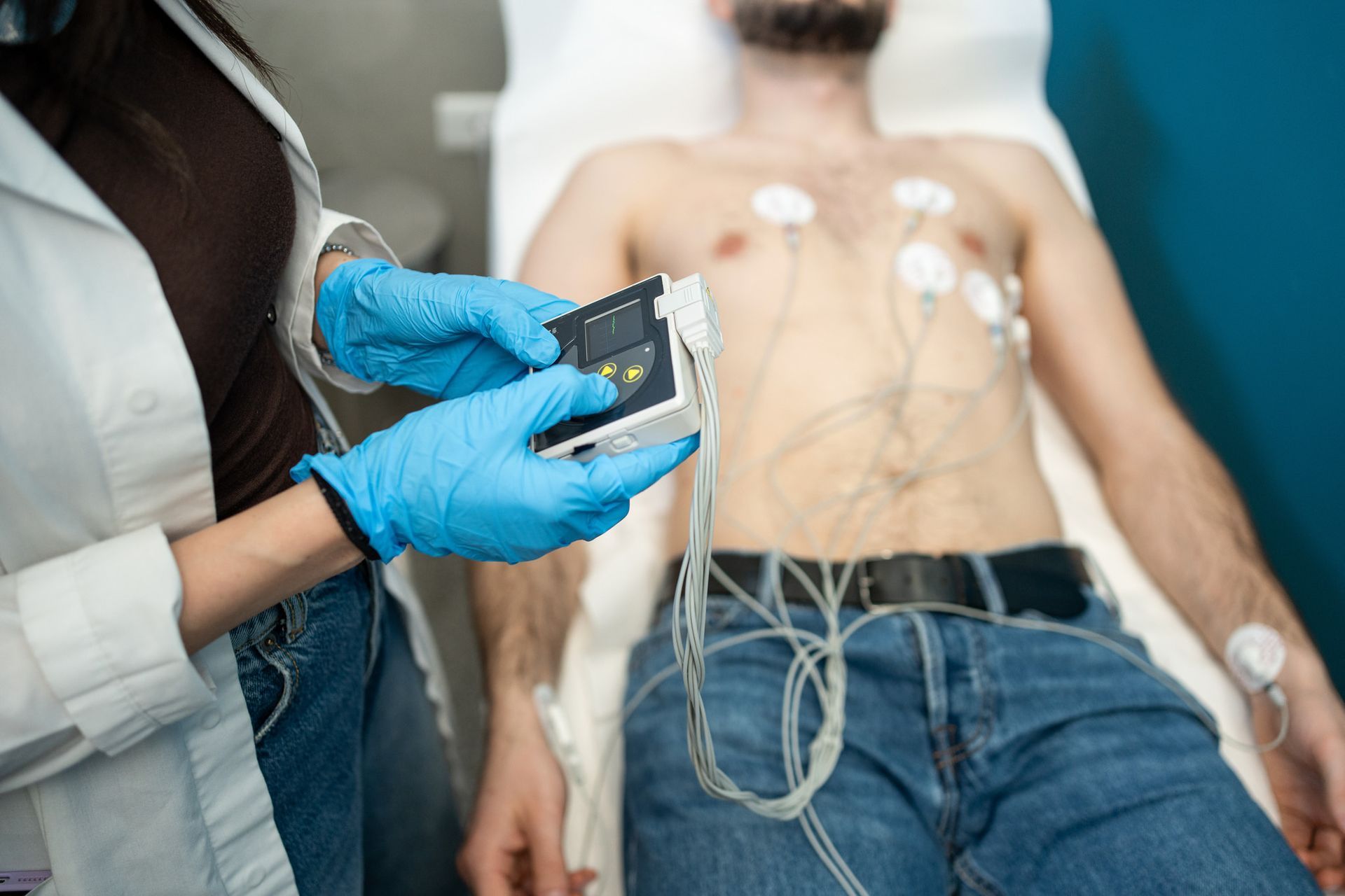 Farmacista con i guanti che tiene un dispositivo portatile sul torace di un paziente con gli elettrodi per l'ECG collegati.
