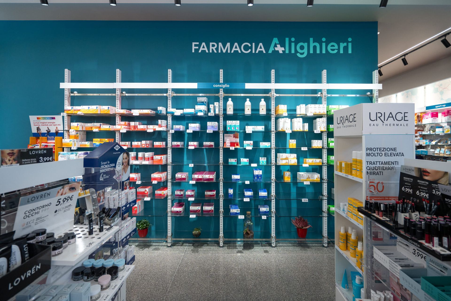 Interno della farmacia, gli scaffali pieni di prodotti fiancheggiano una parete color verde acqua con la scritta