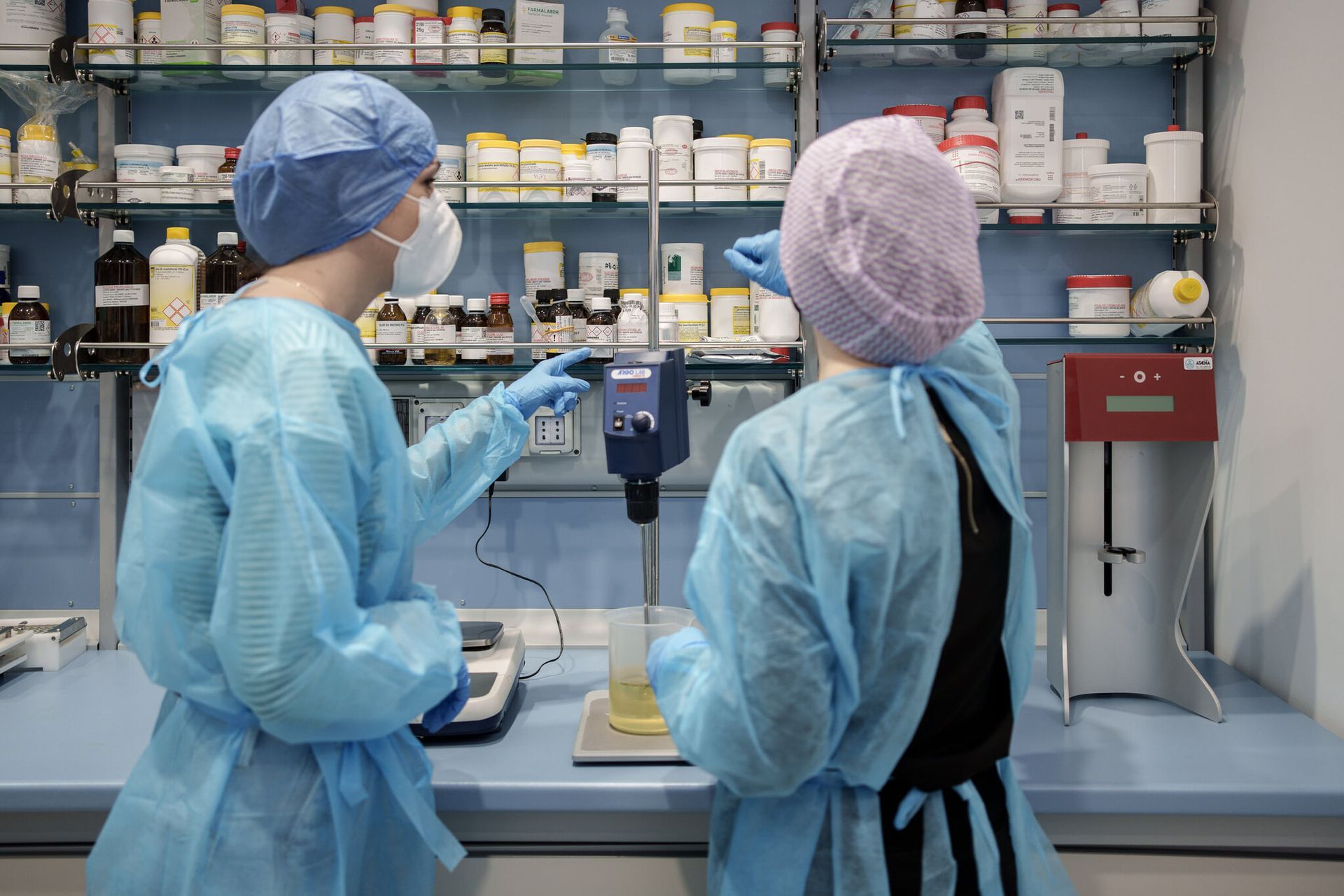 Due tecnici di laboratorio con indumenti protettivi blu lavorano a un banco di laboratorio con attrezzature e materiali.