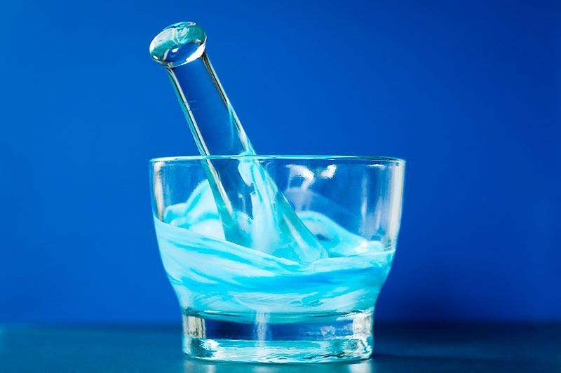 Un mortero de vidrio lleno de líquido azul y una cuchara.