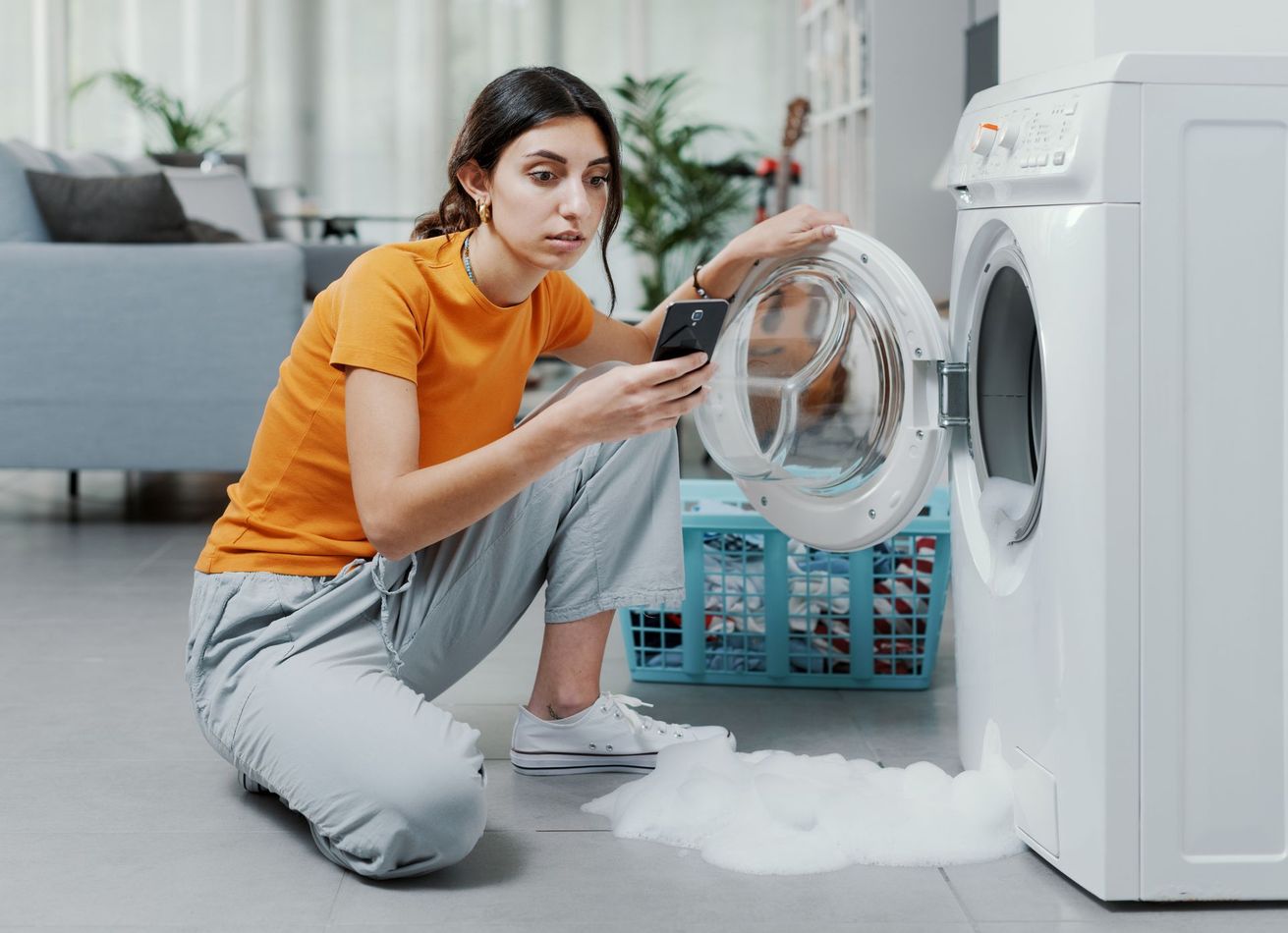 Une femme devant une machine à laver en panne qui cherche un dépanneur