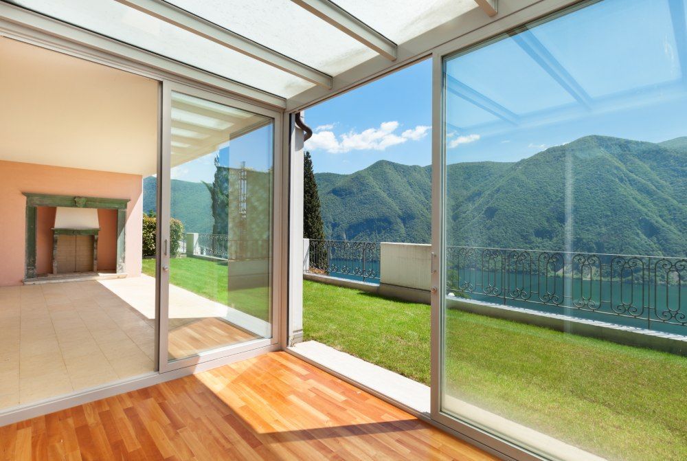 Bright modern room opening to a green terrace and mountain view through large glass doors.
