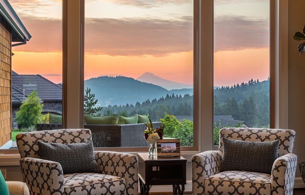 Cozy living room chairs by a window overlooking a sunset over misty mountains and forest