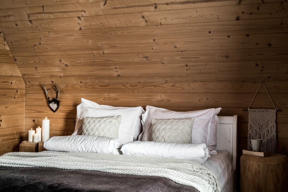 Cozy bedroom with a wooden plank wall, white bedding, candles, and rustic decor
