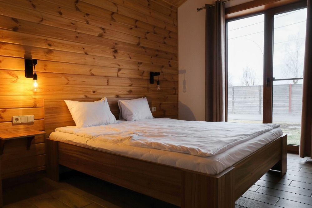 Cozy wood-paneled bedroom with a bed, warm lamp, and large window overlooking snow outside