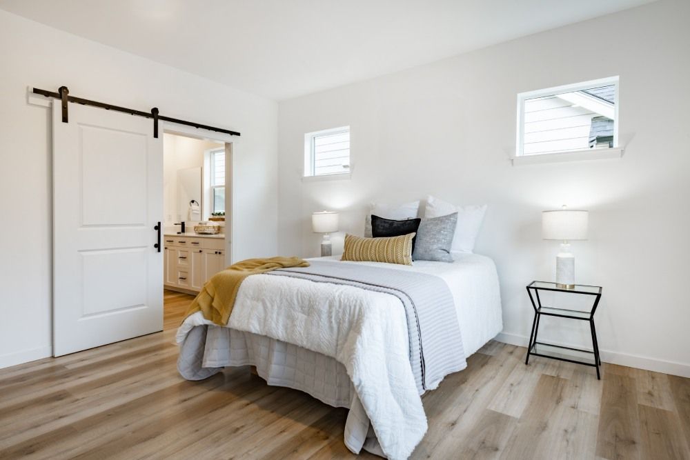 Bright bedroom with a white bed, wood floors, sliding barn door, and two small windows