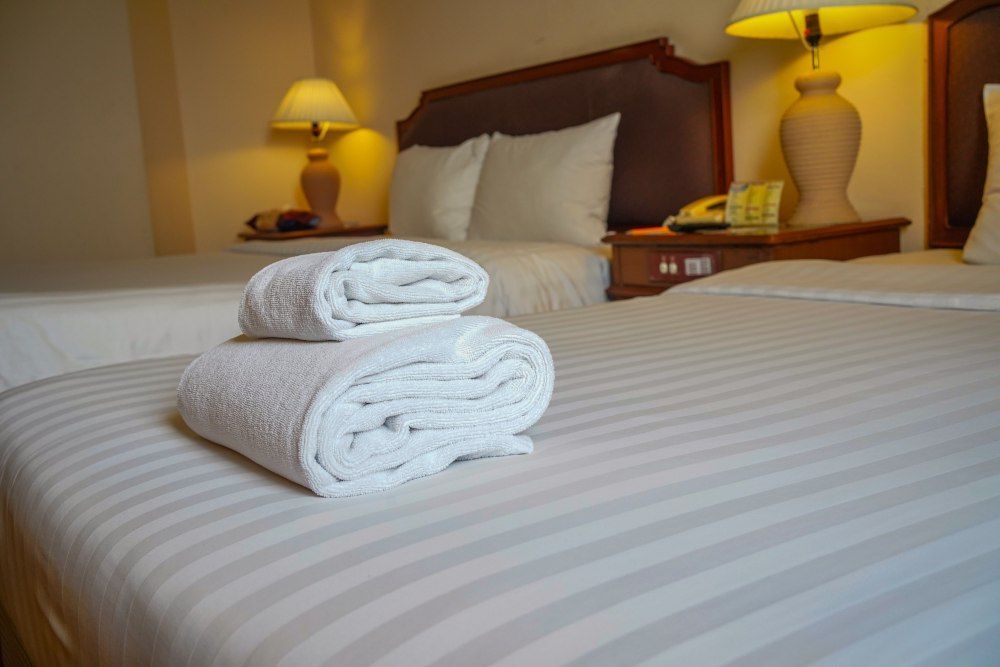 Neatly made hotel bed with two rolled white towels and bedside lamps