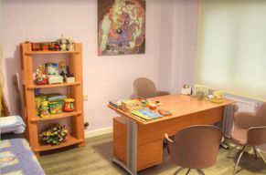 Una habitación con un escritorio, sillas, un estante y un cuadro en la pared.