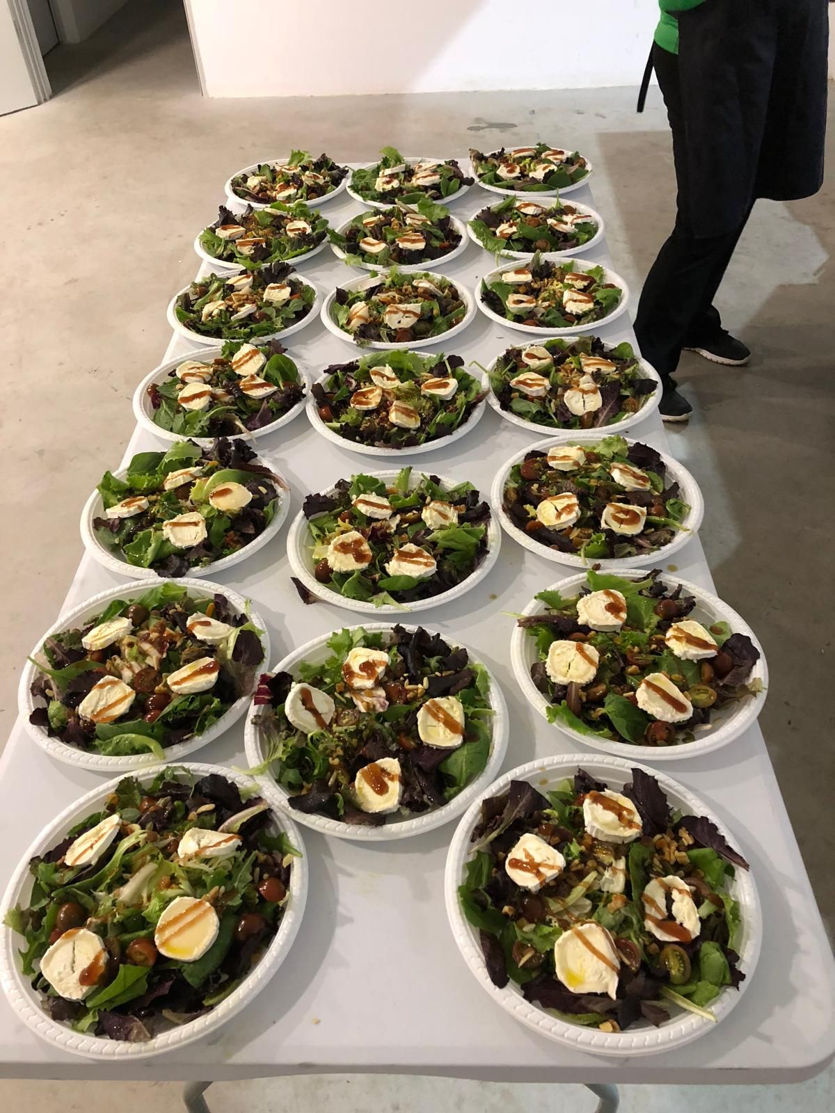 Una mesa cubierta con platos de ensalada y una persona de pie al fondo.