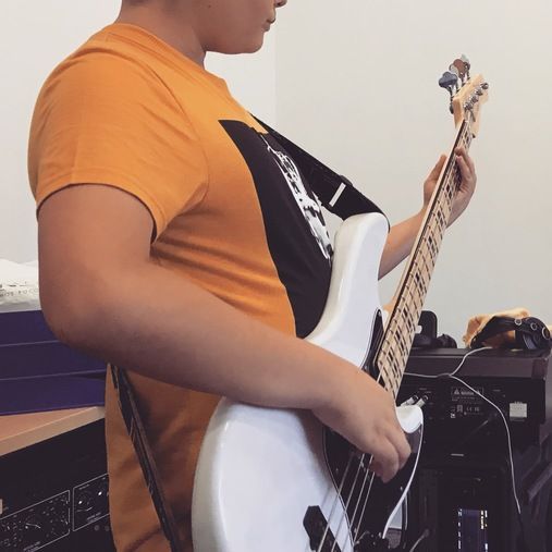 Un hombre con una camisa naranja toca una guitarra blanca.