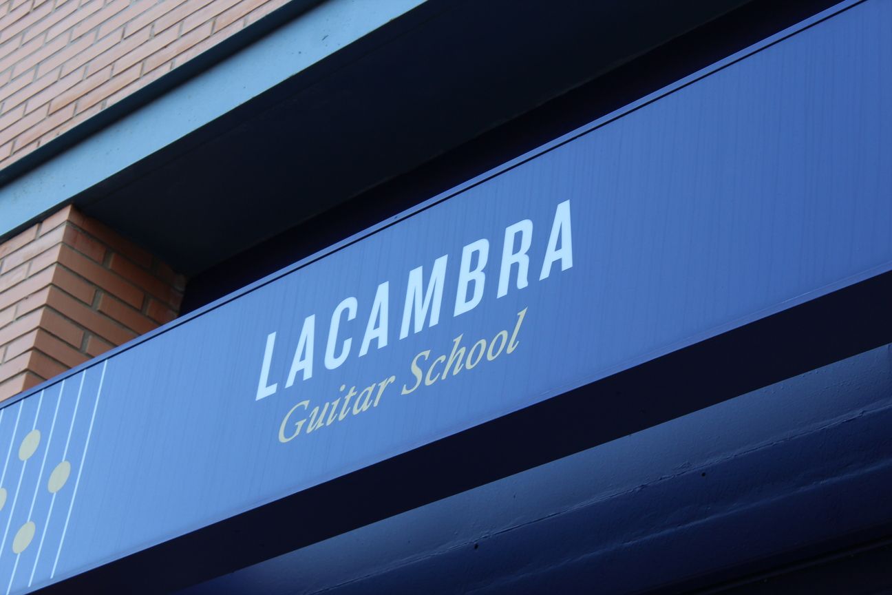 Un cartel azul que dice escuela de guitarra lacambra