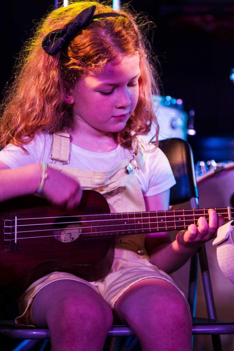 Una niña está sentada en una silla tocando una guitarra.