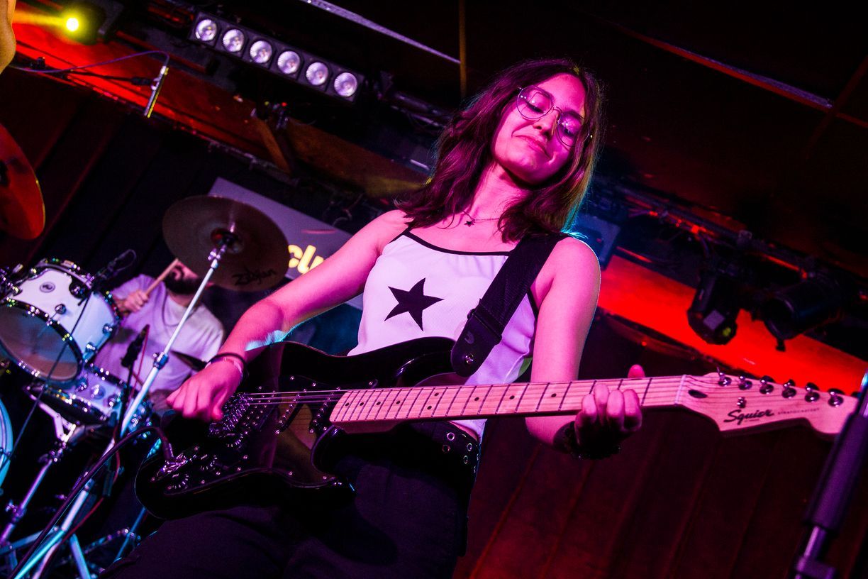 Una mujer está tocando una guitarra en el escenario delante de una batería.