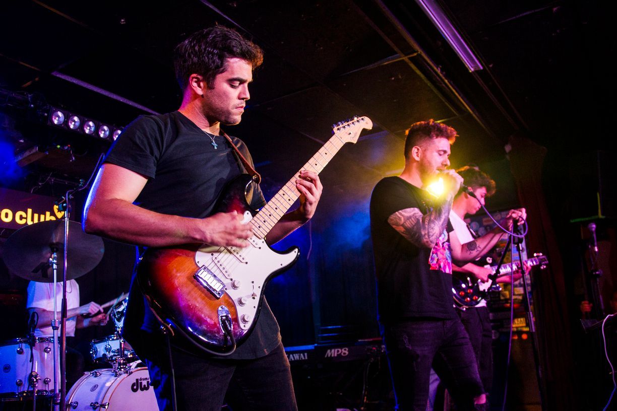 Un hombre toca una guitarra en el escenario mientras otro hombre canta en un micrófono.