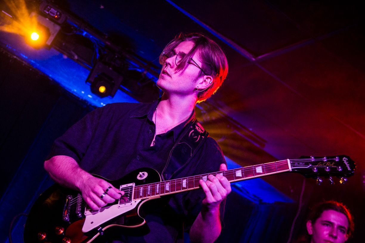 Un hombre está tocando una guitarra en un escenario en una habitación oscura.