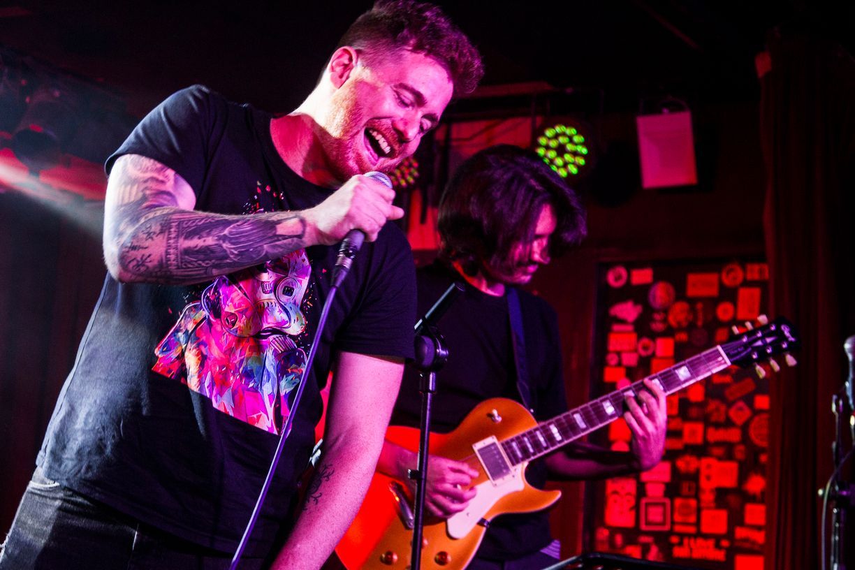 Un hombre canta en un micrófono mientras otro hombre toca una guitarra en el escenario.