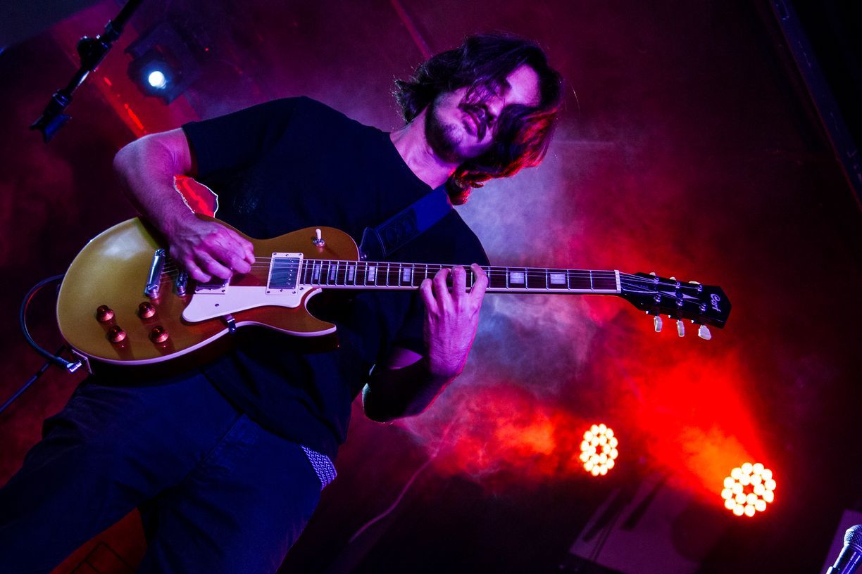 Un hombre está tocando una guitarra en el escenario en una habitación oscura.