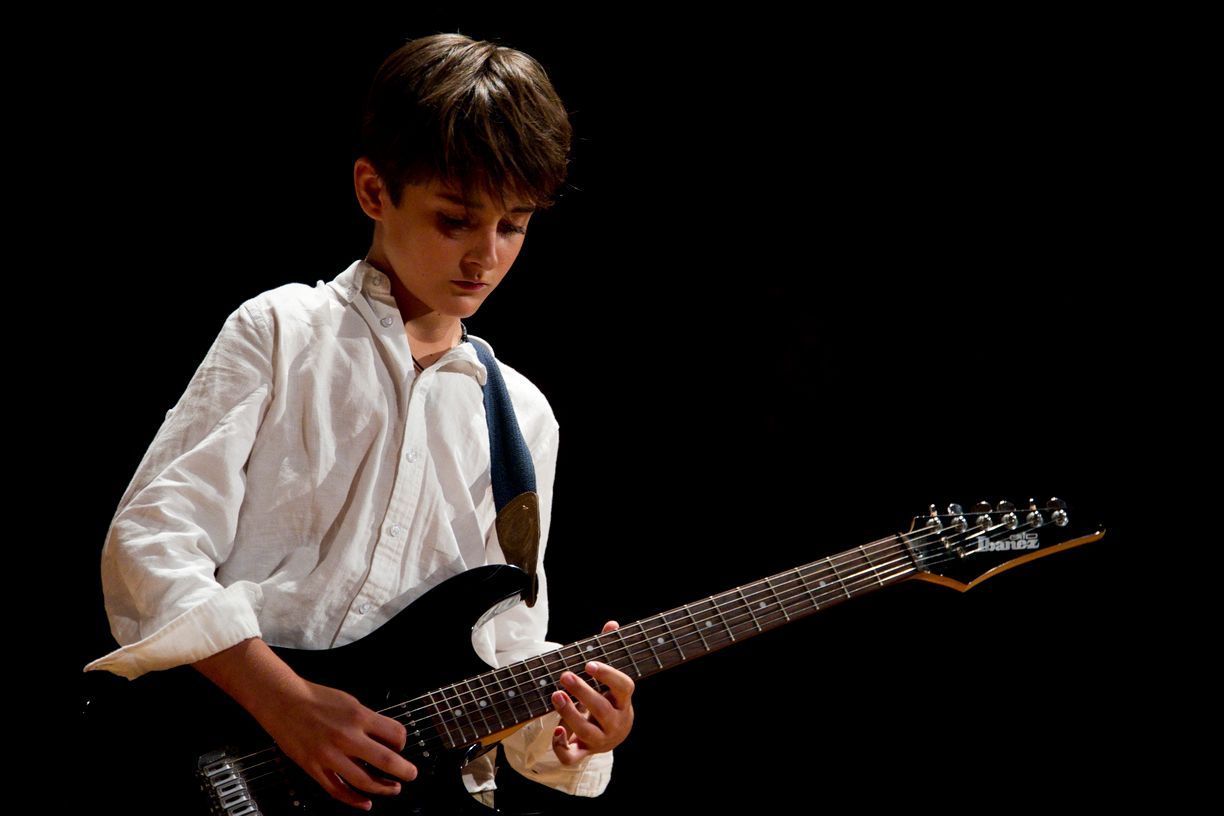 Un niño con camisa blanca y corbata está tocando una guitarra eléctrica.