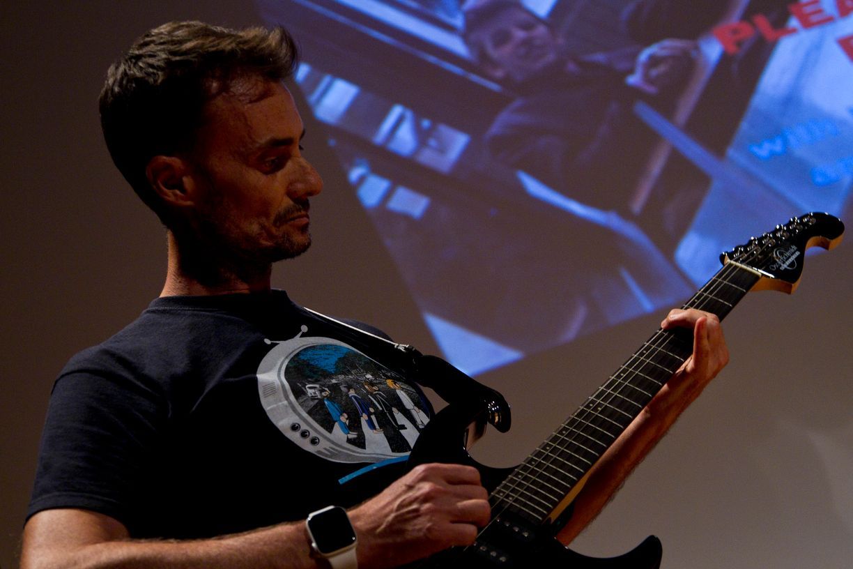 Un hombre con una camisa negra está tocando una guitarra eléctrica.