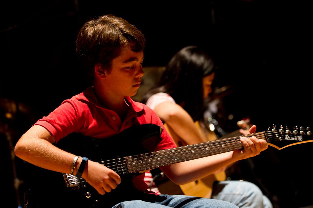 Un niño con una camisa roja está tocando una guitarra eléctrica.