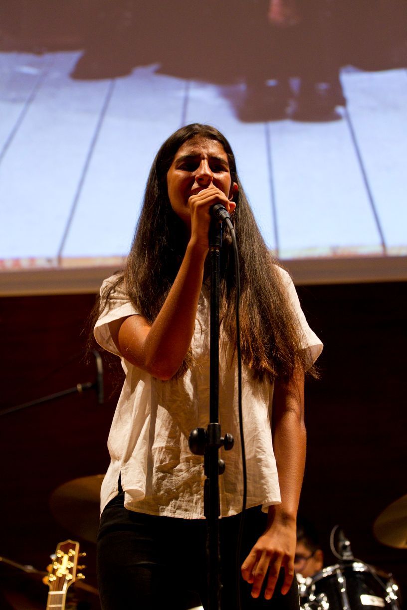 Una mujer cantando en un micrófono con un piano de fondo.