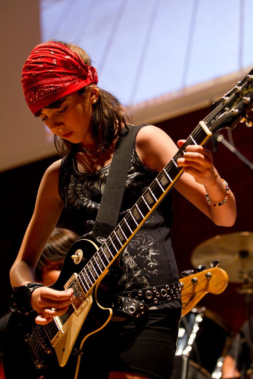 Una mujer que lleva un pañuelo rojo está tocando una guitarra.